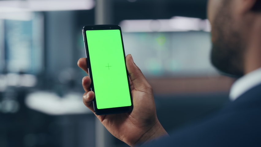 Black Businessman with Green Screen Chroma Key Smartphone in Office. African-American Businessperson using Internet, Social Media, Online Shopping with Mobile Phone Device. Over Shoulder | Shutterstock HD Video #1079293130
