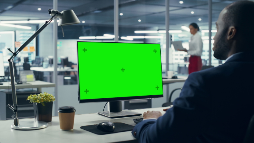 Successful Black Businessman Sitting at Desk Working on Green Screen Laptop Computer in Office. African American Businessperson using Chroma Key Display. Over Shoulder Zoom In Royalty-Free Stock Footage #1079293142