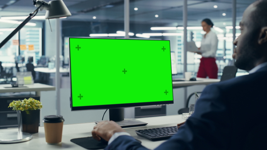 Successful Black Businessman Sitting at Desk Working on Green Screen Laptop Computer in Office. African American Businessperson using Chroma Key Display. Over Shoulder Static Shot Royalty-Free Stock Footage #1079293145