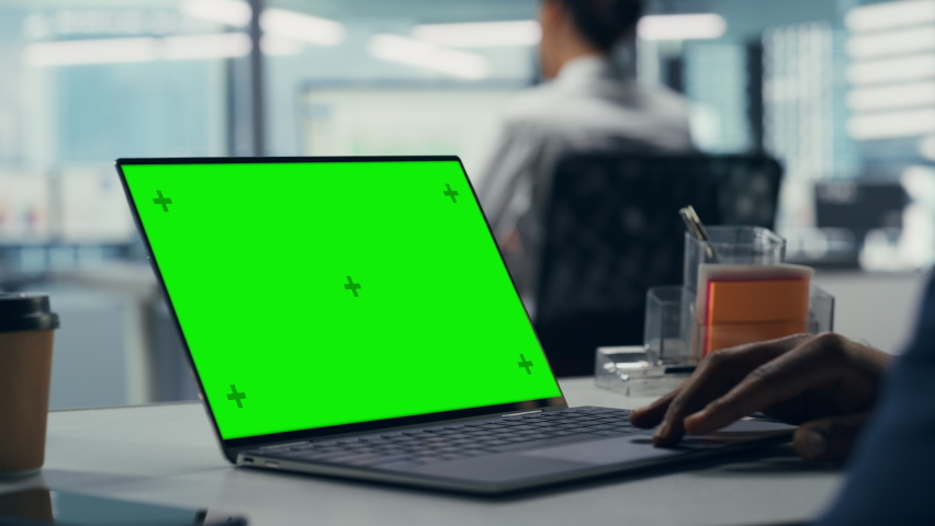 Successful Black Businessman Sitting at Desk Working on Green Screen Laptop in Office. African American Businessperson using Touch Pad on Chroma Key Computer. Over Shoulder Static Shot Focus on Hand Royalty-Free Stock Footage #1079293148
