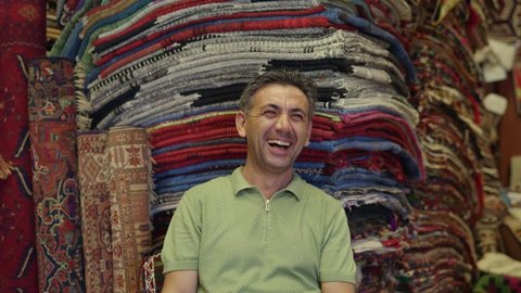 Turkish carpet seller in the carpet shop. The seller, sitting among the colorful authentic carpets, smiles at the camera. Traditional seller portrait. 