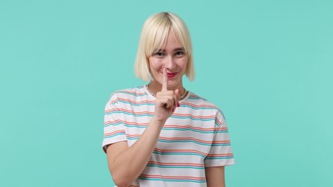 Secret young blonde short haircut woman 20s years old wears striped t-shirt look aside say hush be quiet with finger on lips shhh gesture isolated on pastel plain light blue background studio portrait