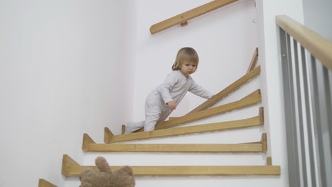 Baby child crawling down on stairs to take teddy bear toy, rescue friend, throwing away toy, playful kid
