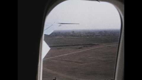 1970s: Onboard airplane, looking out window as it lands. Airplane taxis on runway to airport. Large picture of Mao Zedong on building. Soldiers stand in rows waiting for plane.