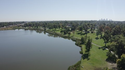 Hovering drone shot on the edge of Berkeley Lake, in full summer sunlight at mid-day, with the Denver skyline and I-70 traffic in the background, captured by a drone in 4K resolution.