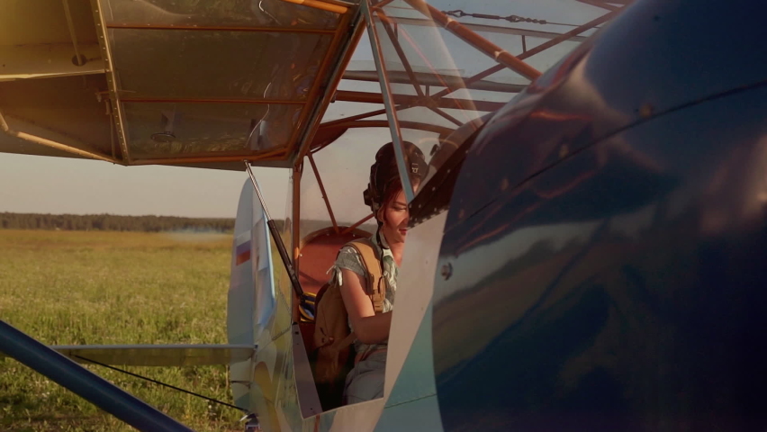 Young adventurous woman pilot in old airplane at summer sunset. Freedom, extreme and feminism concept. Breathtaking adventure in the air. Proffesional captain girl preparing for flight and skydiving