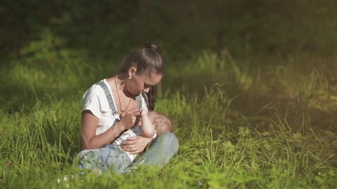 Young and happy mother feeding her baby in the summer on the nature outdoors. Breastfeeding and motherhood lifestyle. Natural mom milk best for newborn. Toddler and mother, togetherness and innocence
