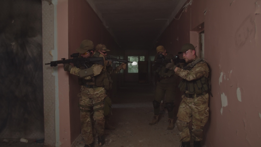 Counter-terrorism squad in combat gear, weapon in firing position, walking along corridor of building, checking rooms for presence of enemies. Teamwork of professional army soldiers on assault mission