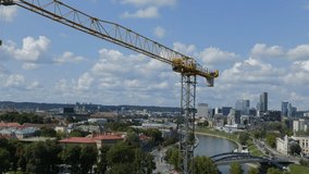 Ungraded: Tower construction crane stands motionless, swaying in the wind on background of aerial city view of Vilnius, Lithuania. Ungraded H.264 from camera without re-encoding.
