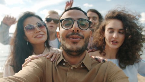 POV portrait of cheerful Arab man dancing outdoors with group of friends laughing enjoying beach party having fun together. Lifestyle and youth concept.