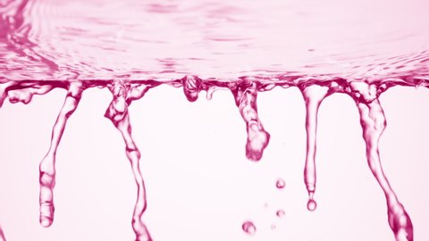 Pink fluid is flowing down from glass surface on pale pink background | Background shot for body care cosmetics advertising