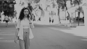 a young curly-haired girl walks down the street, smiles and speaks on the phone. black and white video.