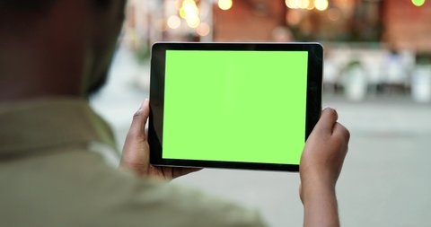Male hands holding tablet with green screen. Guy using mobile phone while walking in the autumn street. Back view shot. Chroma key, close up man hand holding device with vertical green screen