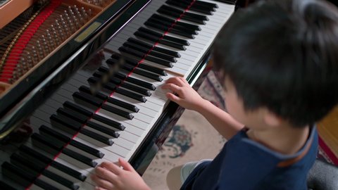 Top view of Asia boy playing grand piano in the living room and selective focus on hand. Practice and learning online. Hobby and study at home. Happy day and family concept. Activity and lifestyle.