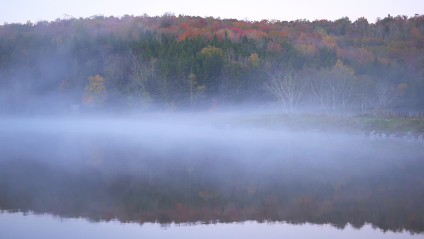 Spruce Knob Lake in West Virginia at sunrise with landscape view of water and forest trees in autumn fall season and moving vapor fog mist closeup
