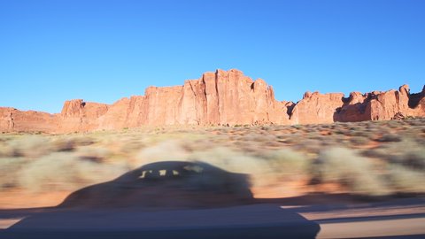 Pov point of view panning driving vehicle side view shot on arches scenic drive at Arches National Park in Moab, Utah at sunrise with canyons rock formations and car shadow on road trip