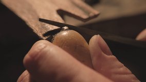 A jeweler polishes a product with a file in a dark workshop. A jeweler makes a product in his workshop by performing various processes. Close-up. Macro. The jeweler installs the piece in the clip