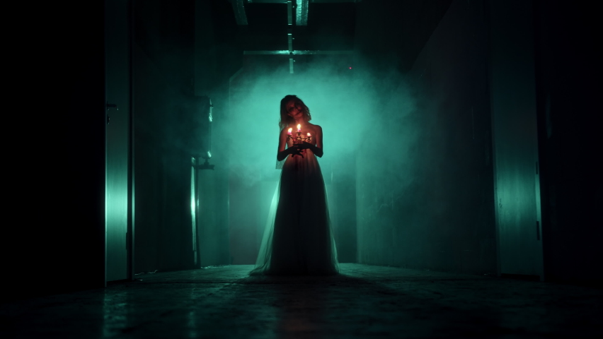 Zombie woman holding burning candles in dark corridor. Creepy dead bride wearing wedding dress and veil. Bloody scary smile. Deceased fiancee returned to life. Halloween, usa holiday.