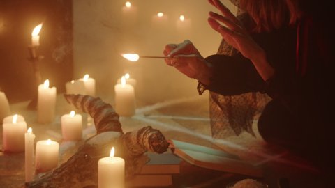 Witch woman lighting candles while sitting in pentagram circle. Evil sorceress preparing for making rite and sacrifices at night, using black witchcraft and cow skull. Full moon, Halloween concept. 