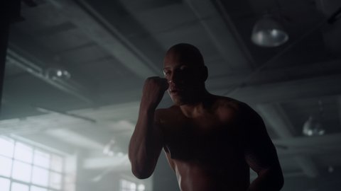 Shirtless sportsman boxing drills to build up hand speed. African american man with muscular body punching air during boxing training. Male boxer doing intense workout in loft building