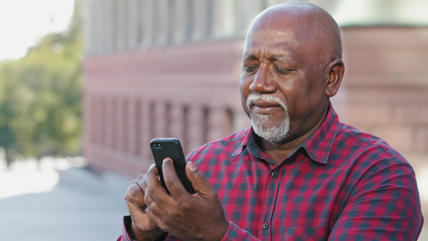 Smiling focused senior black grandfather typing sms message, looking at smartphone screen, african american mature male elderly man communicating on social networks using mobile phone, sharing news Royalty-Free Stock Footage #1079348030