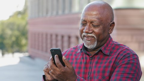 Smiling focused senior black grandfather typing sms message, looking at smartphone screen, african american mature male elderly man communicating on social networks using mobile phone, sharing news