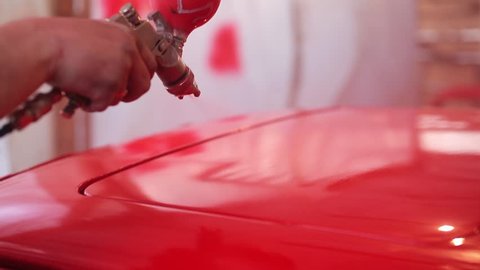 Painter paints the red car in garage.