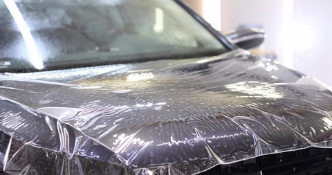 Man repairman wrapping protective vinyl film over car 4k movie