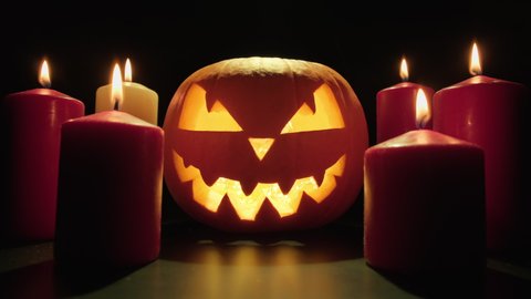 Scary glowing face of Halloween pumpkin. Pumpkin with burning candles around it. Traditional Halloween symbol. Pumpkin glows on Halloween night. Halloween concept in 4K, UHD