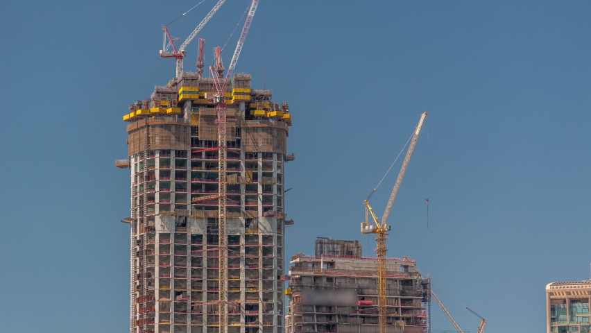 High multi-storey buildings under construction and many cranes timelapse. Active work at construction site of new towers and skyscrapers. Blue sky