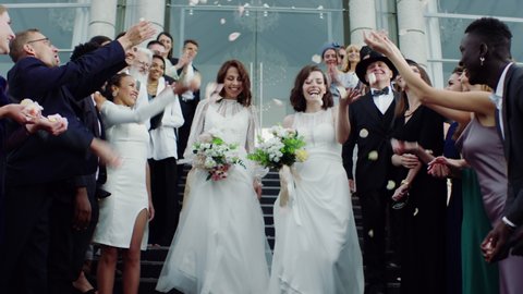 Candid shot of two female lesbian LGBT brides walking down the stairs during their wedding ceremony as guests throwing rose petals. Shot with 2x anamorphic lens
