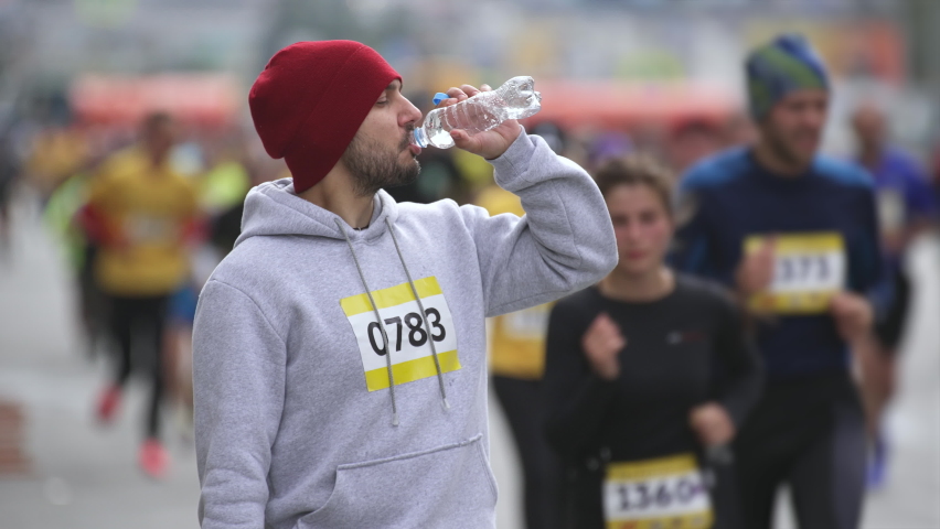 Portrait face of drinking water, looking at camera, tired athlete. Crowd on marathon running event. Groups of racers, marathoners run on active occasion. Athletic sportsman stands on triathlon track.