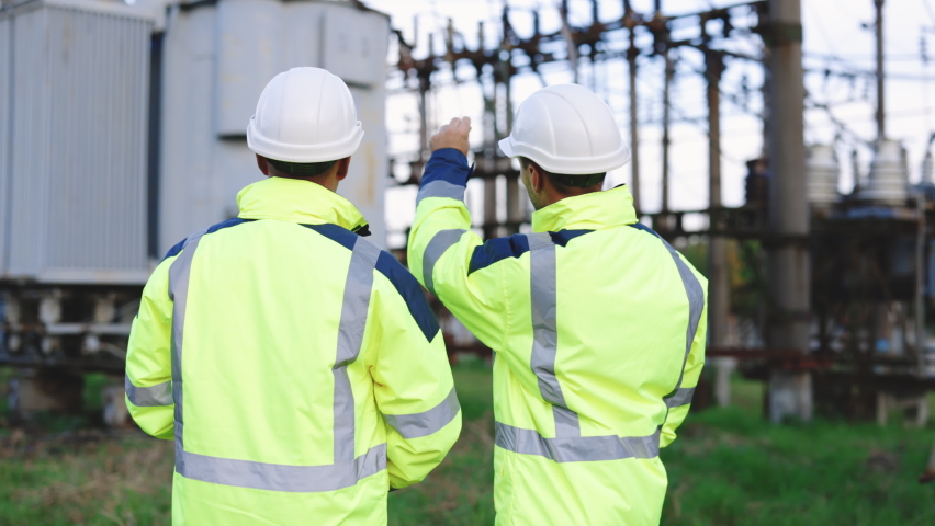 Two Diverse Professional Engineers Wearing Safety Uniform and Hard Hats Working on high-voltage power station. Technician and male Worker Talking on a Meeting