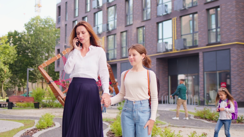 Young handsome mom take her daughter to school. Beautiful mother talk on telephone and pay no attention on girl.