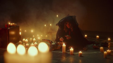 Witch woman lighting candles while sitting in pentagram circle. Evil sorceress preparing for making rite and sacrifices at night, using black witchcraft and cow skull. Full moon, Halloween concept. 