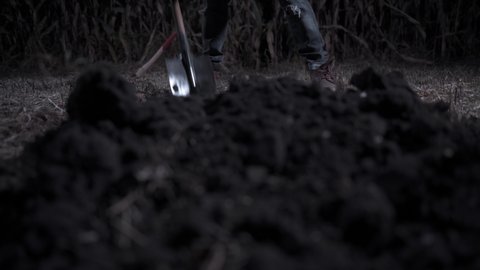 Killer digs grave at night. Young scary man digs hole in field. Close up front view.