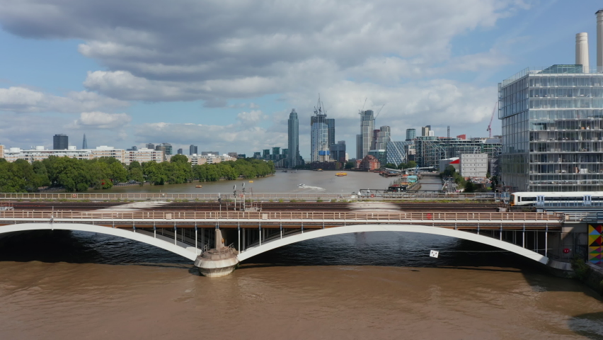 Forwards fly over train driving on bridge across Thames river. Group of modern skyscrapers in background. London, UK