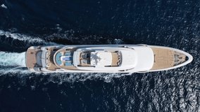 Aerial drone top down video of luxury yacht with wooden deck and helicopter landing pad cruising deep blue Mediterranean sea