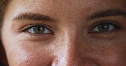 Gaze. Beautiful green eyes of young smiling female looking at camera. Macro view of attractive millennial woman happy face with opened eyes thick eyebrows cute freckles on smooth skin. Cropped closeup