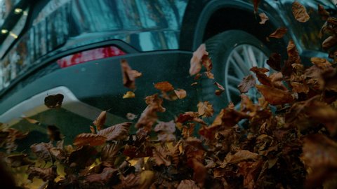 SLOW MOTION, LENS FLARE, LOW ANGLE, CLOSE UP: Big metallic blue SUV drives down a leaf covered forest trail at picturesque autumn sunrise. Scenic shot of an offroad vehicle rising crunchy dry leaves.
