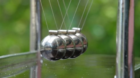 Newton's Cradle metal balls on green nature background, swinging metal balls, Macro shot. Close up.