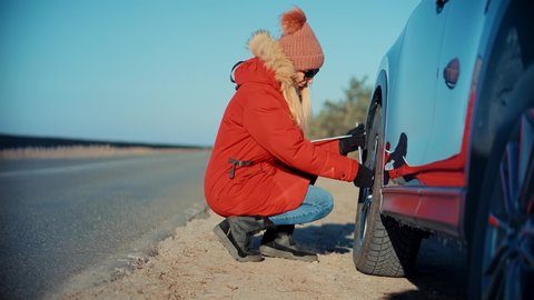 Woman Check Car Tire Pressure. Vehicle Trouble On Road On Vacation Trip. Female Trying Fix Car Tire.Transportation Concept. Problem With Car On Countryside Road. Automobile Repair Inflating Tire Check
