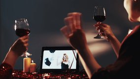 Online toast. Virtual Xmas celebration. Festive video call. Remote New Year party. Happy girls greeting drinking alcohol clinking glasses using tablet at festive night.