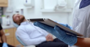 Caucasian female nurse typing on digital tablet while male patient lies on doctors bed 