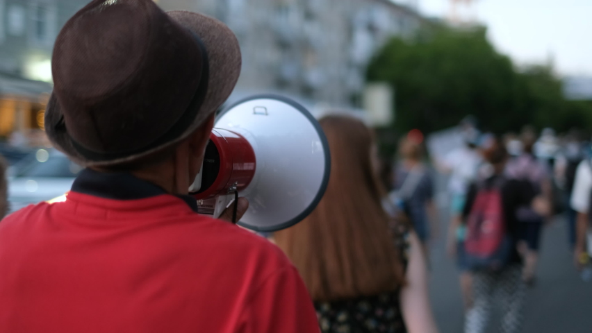 Strike activist demonstrator man on opposition rally riot with megaphone walks. Political protester guy with bullhorn marches in protest crowd. Male rebel speaking on demonstration revolt resistance. Royalty-Free Stock Footage #1079407220
