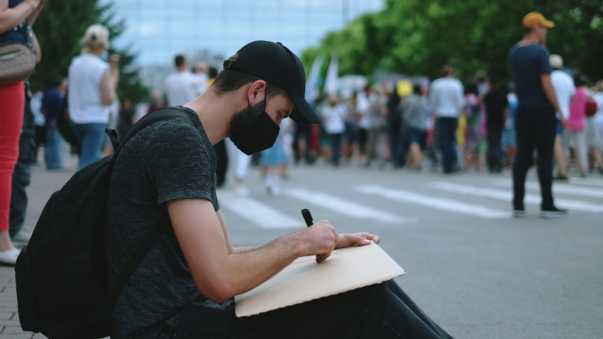 Peaceful protester man on political rally in covid-19 mask draws sign poster. Rebel man on city street revolt, resistance strike. Male picket activist drawing demonstration banner placard protesting. Royalty-Free Stock Footage #1079407241