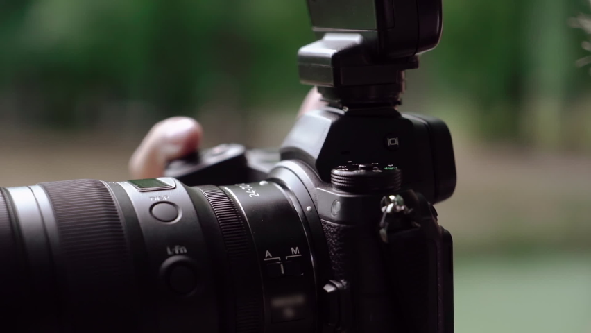 Male photographer takes photographs on a professional camera. A man holds in his hands a camera with an attached synchronizer for the flash using display. Photo session outdoors in park.