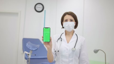  gynecologist shows an iPhone 12 with a chromakey. The doctor in the gynecological office shows mobile phone with green mock up screen. Online consultation with doctor .June 16, 2021 - Moscow, Russia 