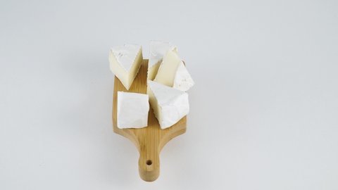 Triangles of goat milk cheese with white mold. Several slices of the famous Camembert Brie cheese on a wooden cutting board rotate. Brie cheese on a white plate.