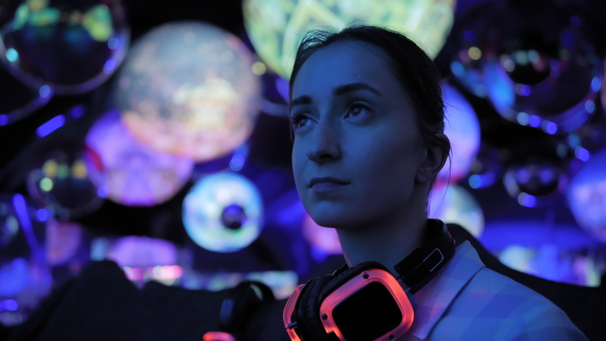 Woman wearing wireless black headphones and looking around in dark room of interactive museum or exhibition with colorful illumination. Immersive, futuristic, entertainment concept Royalty-Free Stock Footage #1079411909